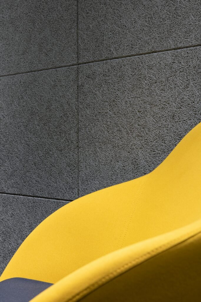 Detail of comfortable bright chair with yellow fabric and cushion placed near gray textured wall in room of modern studio